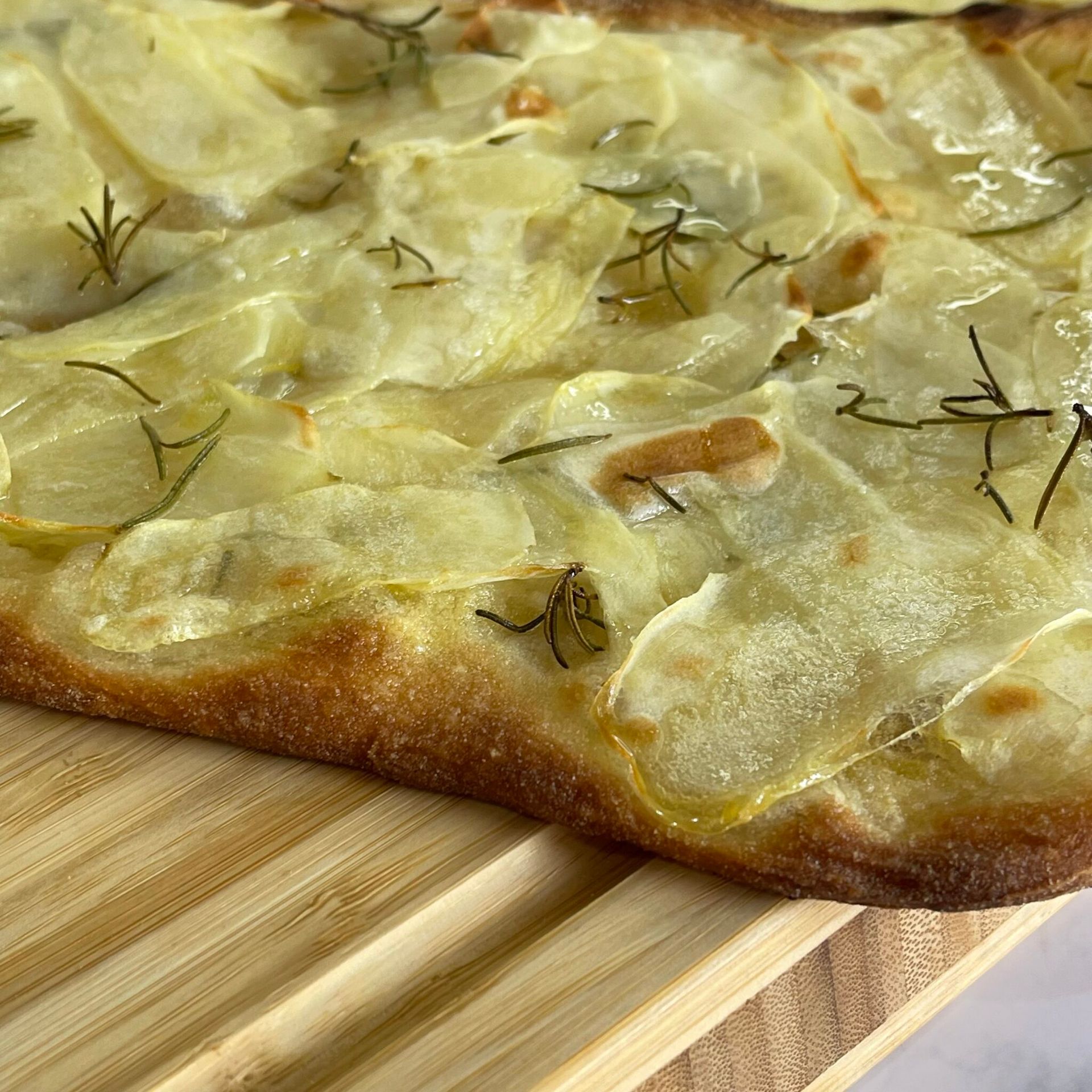 Una pizza con patate e formaggio è appoggiata su un tagliere di legno.