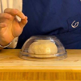 Una persona tiene una cupola di vetro sopra una palla di pasta
