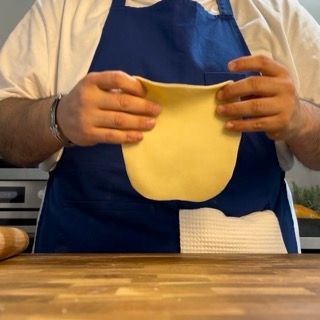 Un uomo con un grembiule blu tiene in mano un pezzo di pasta