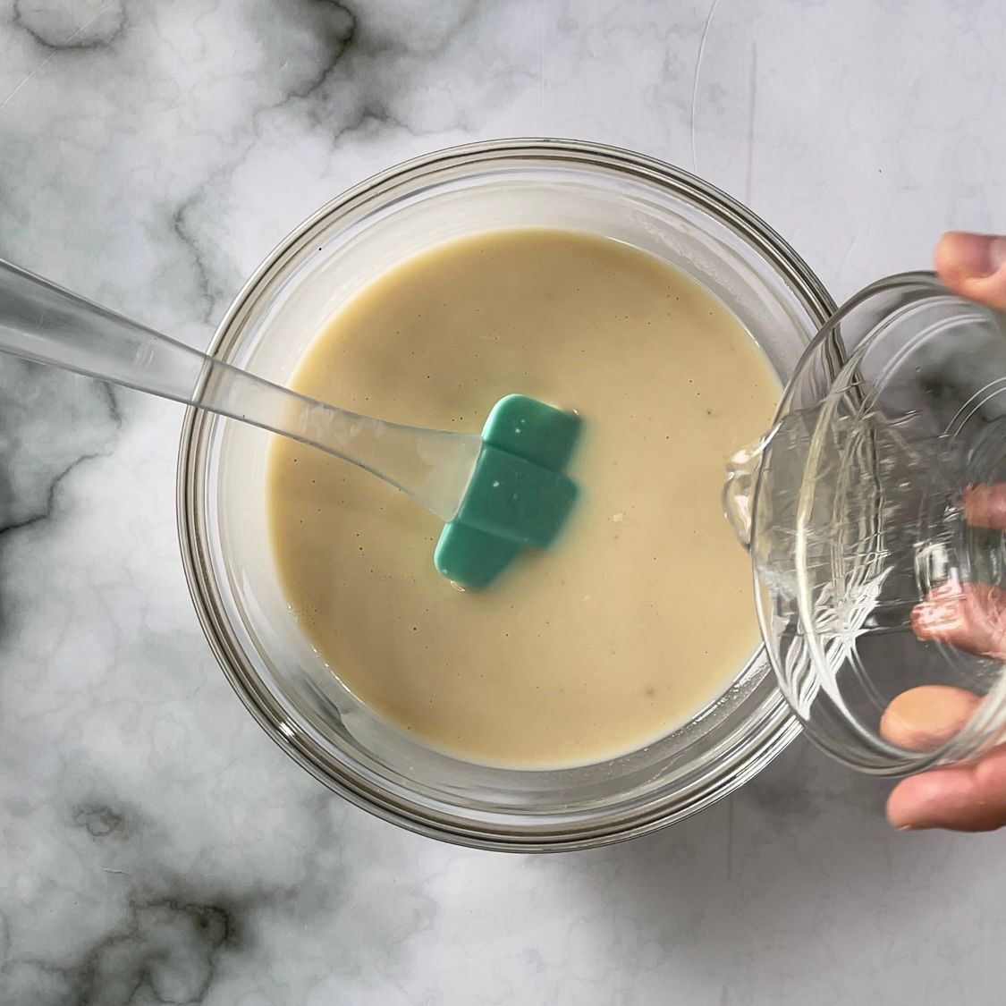 Una persona versa del liquido in una ciotola con una spatola verde.