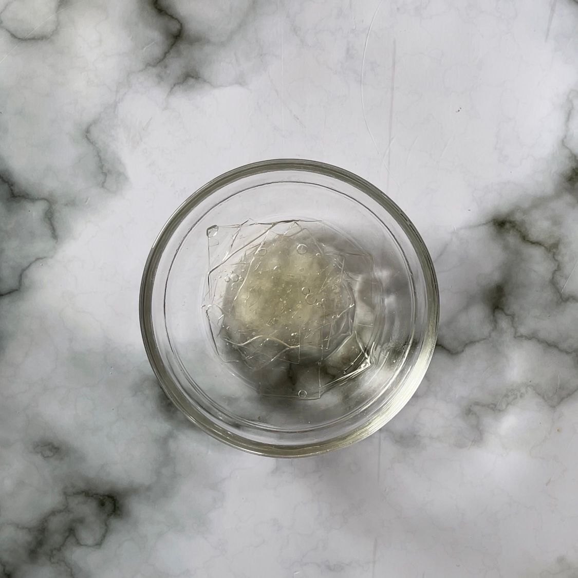Una piccola ciotola di vetro piena di liquido è appoggiata su una superficie di marmo.
