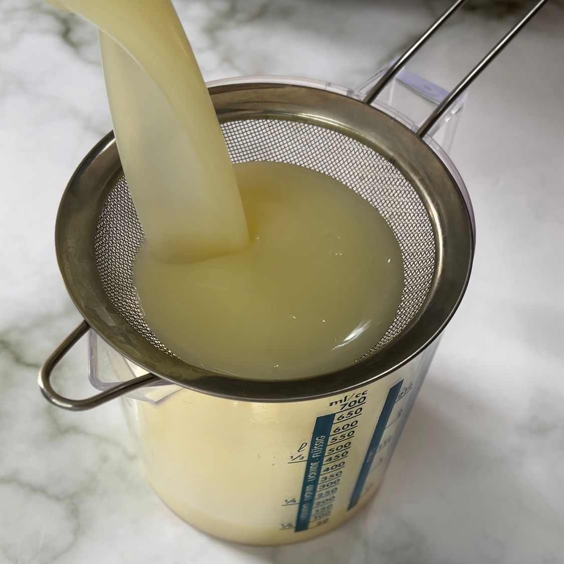 Il liquido viene versato attraverso un colino in una tazza graduata