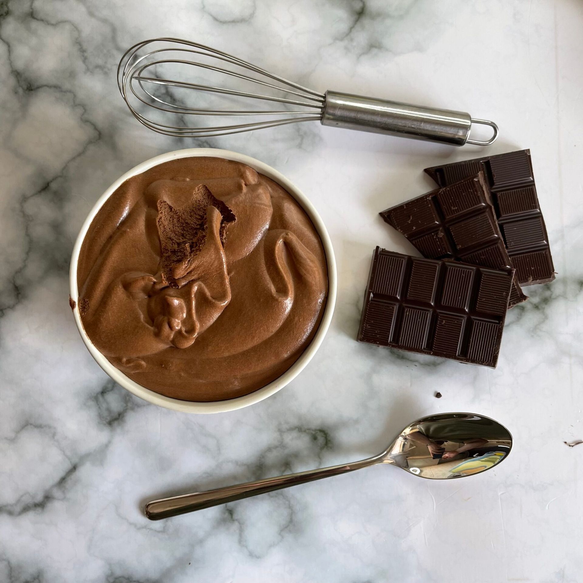 Una ciotola di budino al cioccolato accanto a una frusta e un cucchiaio