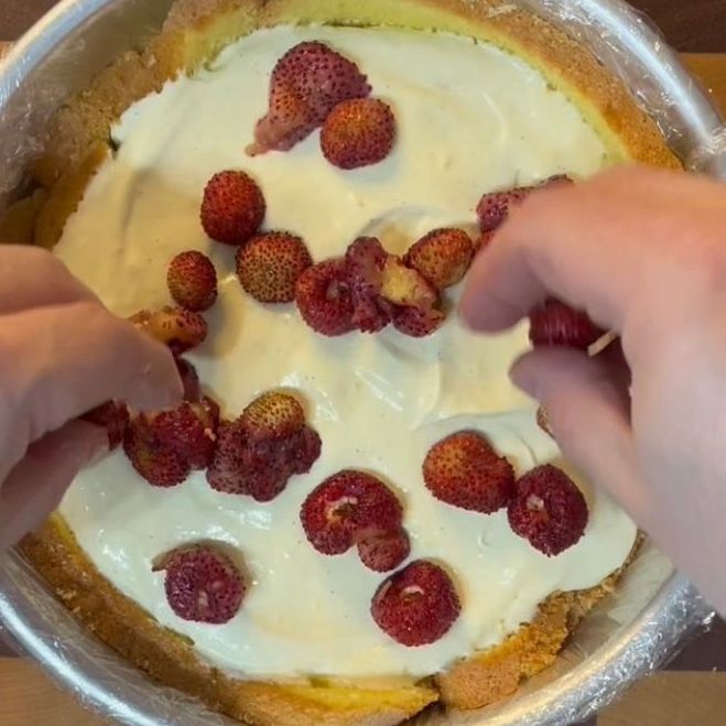 Una persona sta mettendo delle fragole sopra una torta