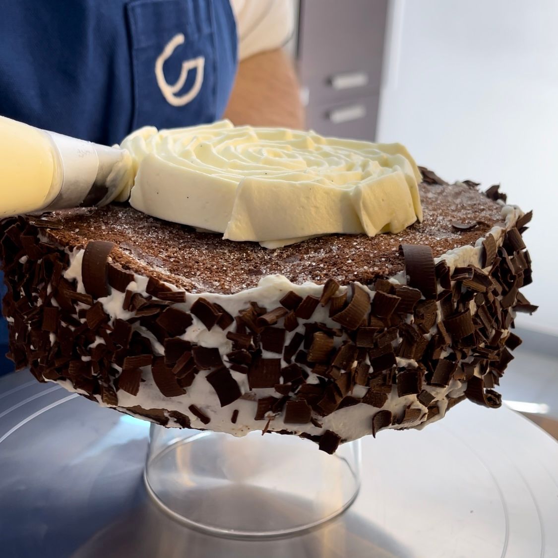 Una persona con un grembiule blu tiene in mano una torta al cioccolato