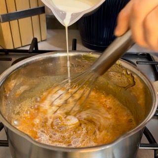 Una persona versa del liquido in una pentola con una frusta.