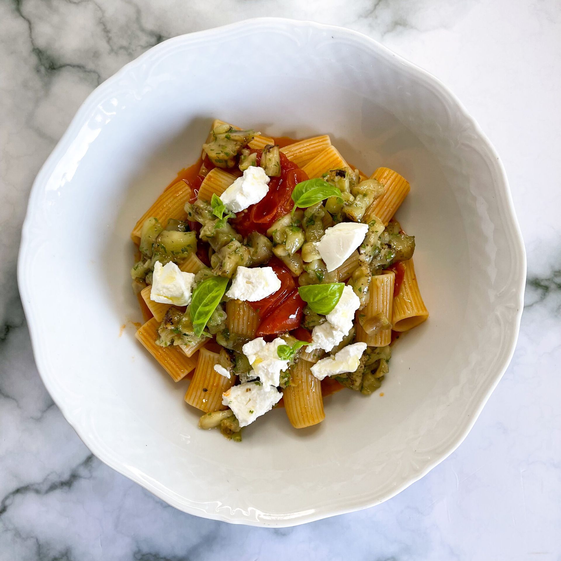 Una ciotola bianca piena di pasta e verdure su un tavolo.