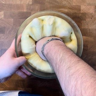 Mani che schiacciano delicatamente l'impasto lievitato per togliere i gas.