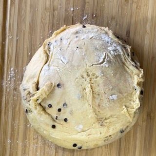 Un pezzo di pasta con gocce di cioccolato è appoggiato su un tagliere di legno.
