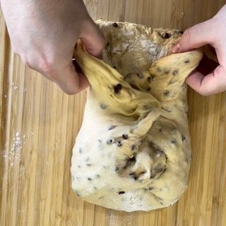 Una persona tiene in mano un pezzo di pasta su un tagliere di legno.