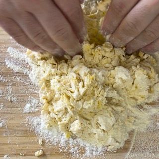 Una persona sta mescolando uova e farina su un tagliere di legno.