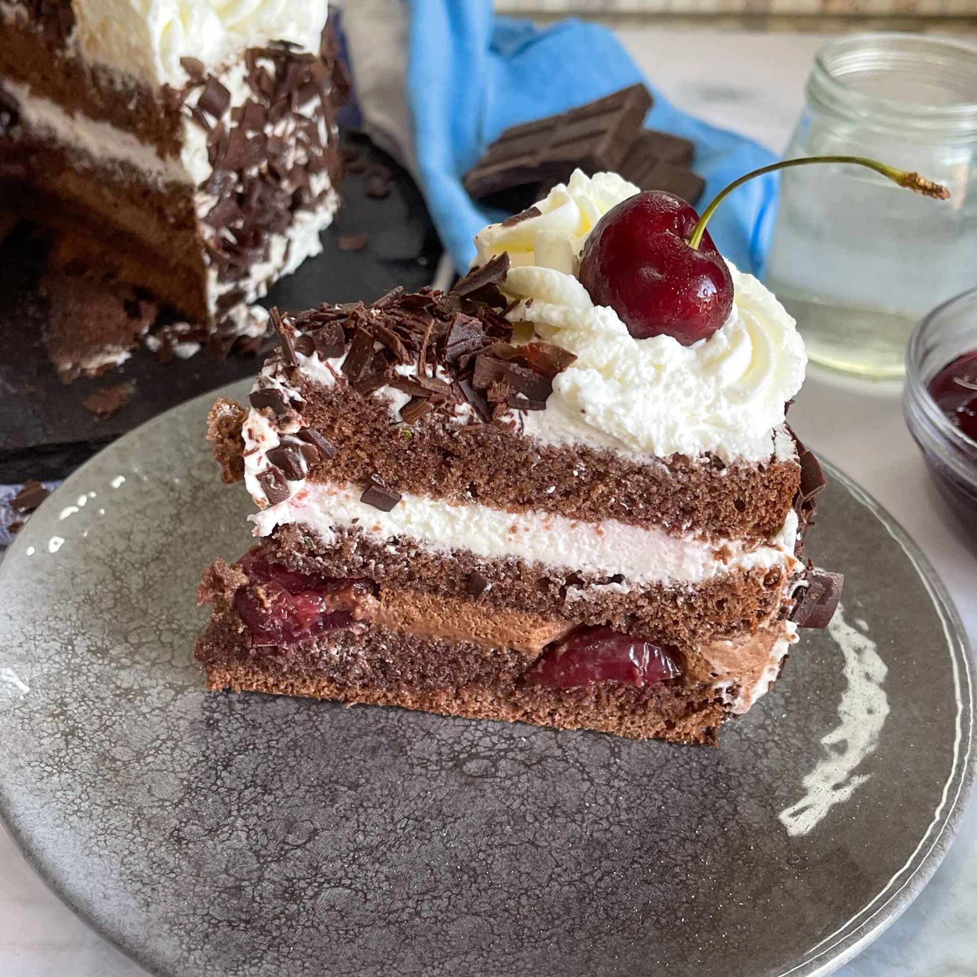 Una fetta di torta Foresta Nera su un piatto con una ciliegia sopra.