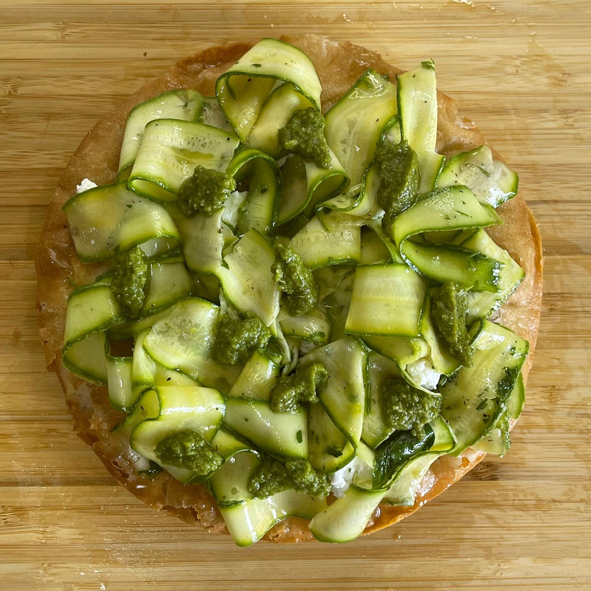 Una pizza con cetrioli e pesto su un tagliere di legno