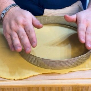 Una persona tiene una padella di metallo sopra un pezzo di pasta