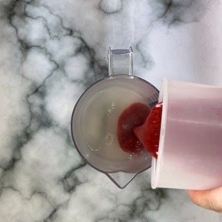 Una persona sta versando la salsa di fragole in un misurino.