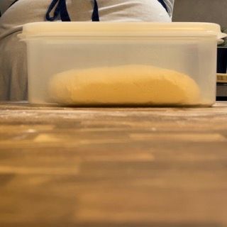 Un contenitore di plastica pieno di impasto è appoggiato su un tavolo di legno.