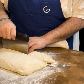 Un uomo che indossa un grembiule blu con la lettera g sopra sta tagliando la pasta