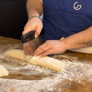 Un uomo che indossa una maglietta blu con la lettera g sopra sta tagliando la pasta
