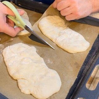 Una persona sta tagliando un pezzo di pasta con le forbici