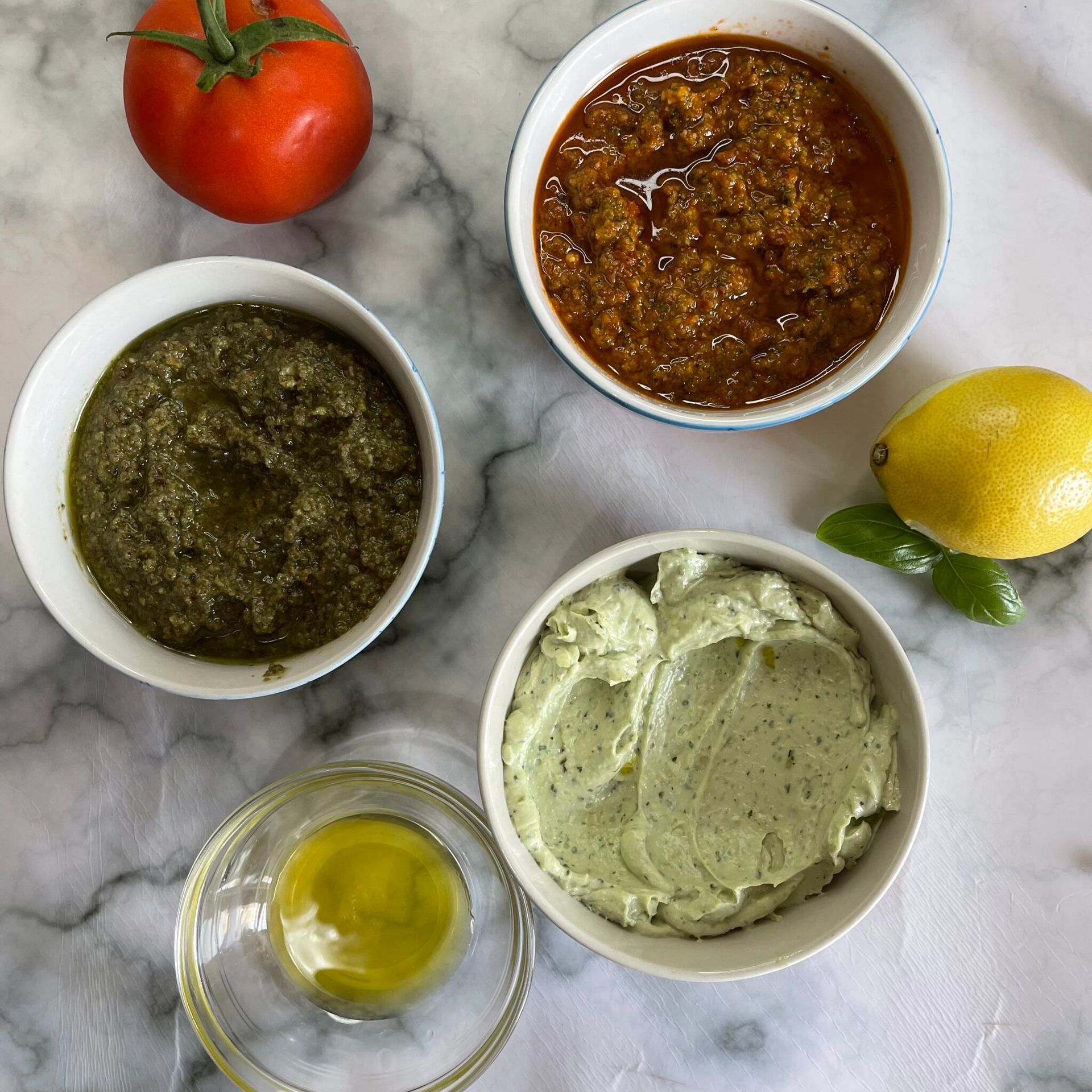 Tre ciotole di salse diverse sono su un tavolo accanto a un pomodoro e un limone