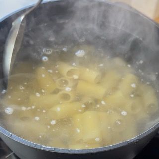 Una pentola di pasta viene cotta nell'acqua bollente con un cucchiaio dentro.