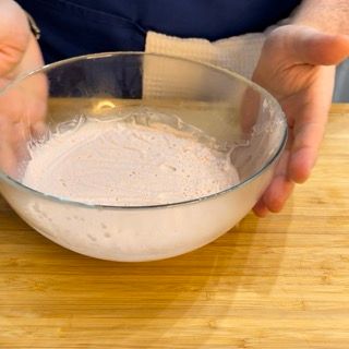 Una persona tiene in mano una ciotola piena di liquido rosa su un tavolo di legno.