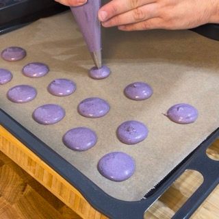 Una persona sta preparando dei biscotti viola su una teglia da forno
