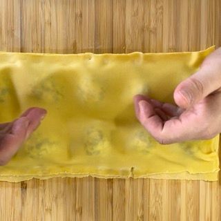 Una persona tiene in mano un pezzo di pasta su un tavolo di legno.