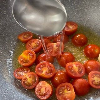 Un cucchiaio versa acqua in una pentola con i pomodori.