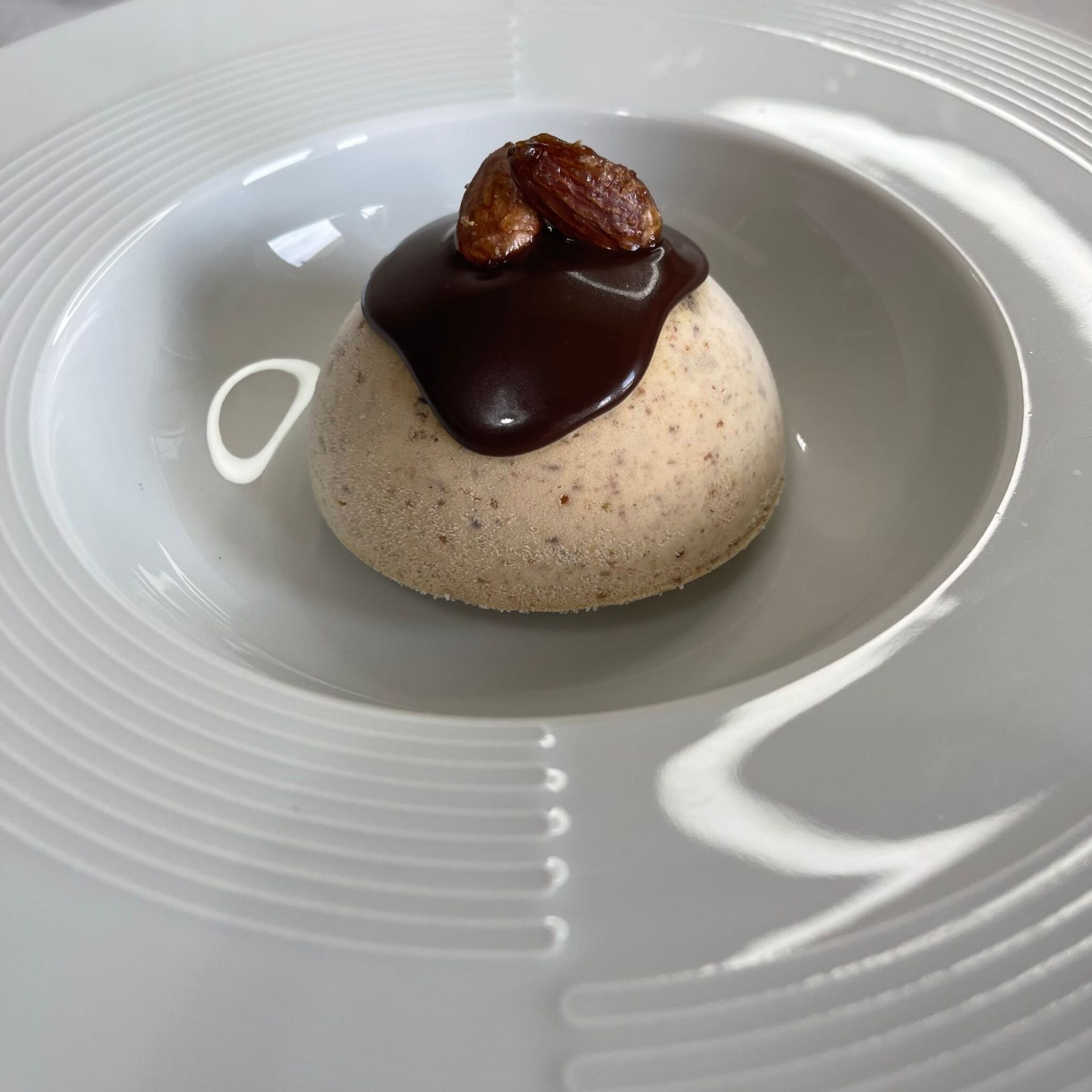 Un piatto bianco sormontato da un dessert con salsa al cioccolato e noci