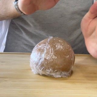 Una persona sta avvolgendo una palla di pasta nella pellicola trasparente.