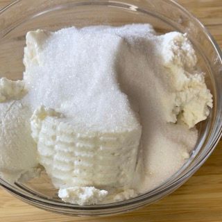 Una ciotola di vetro piena di ricotta e zucchero su un tavolo di legno.