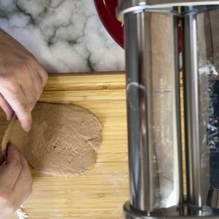 Una persona sta tagliando il pane su un tagliere accanto a una macchina per la pasta.