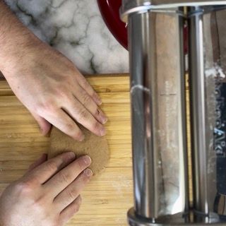 Una persona sta stendendo la pasta su un tagliere accanto a una macchina per la pasta