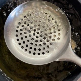 Un colino con dei fori è in una pentola con del liquido.