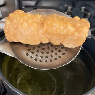 Un cucchiaio tiene un pezzo di cibo sopra una pentola di olio