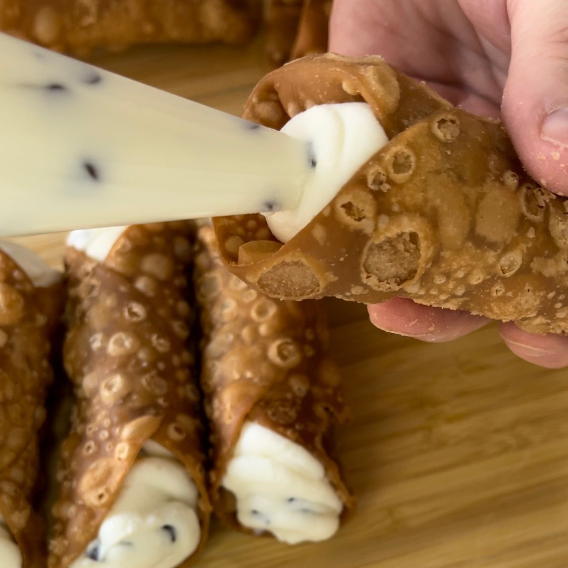 Una persona sta riempiendo un cannolo con panna montata
