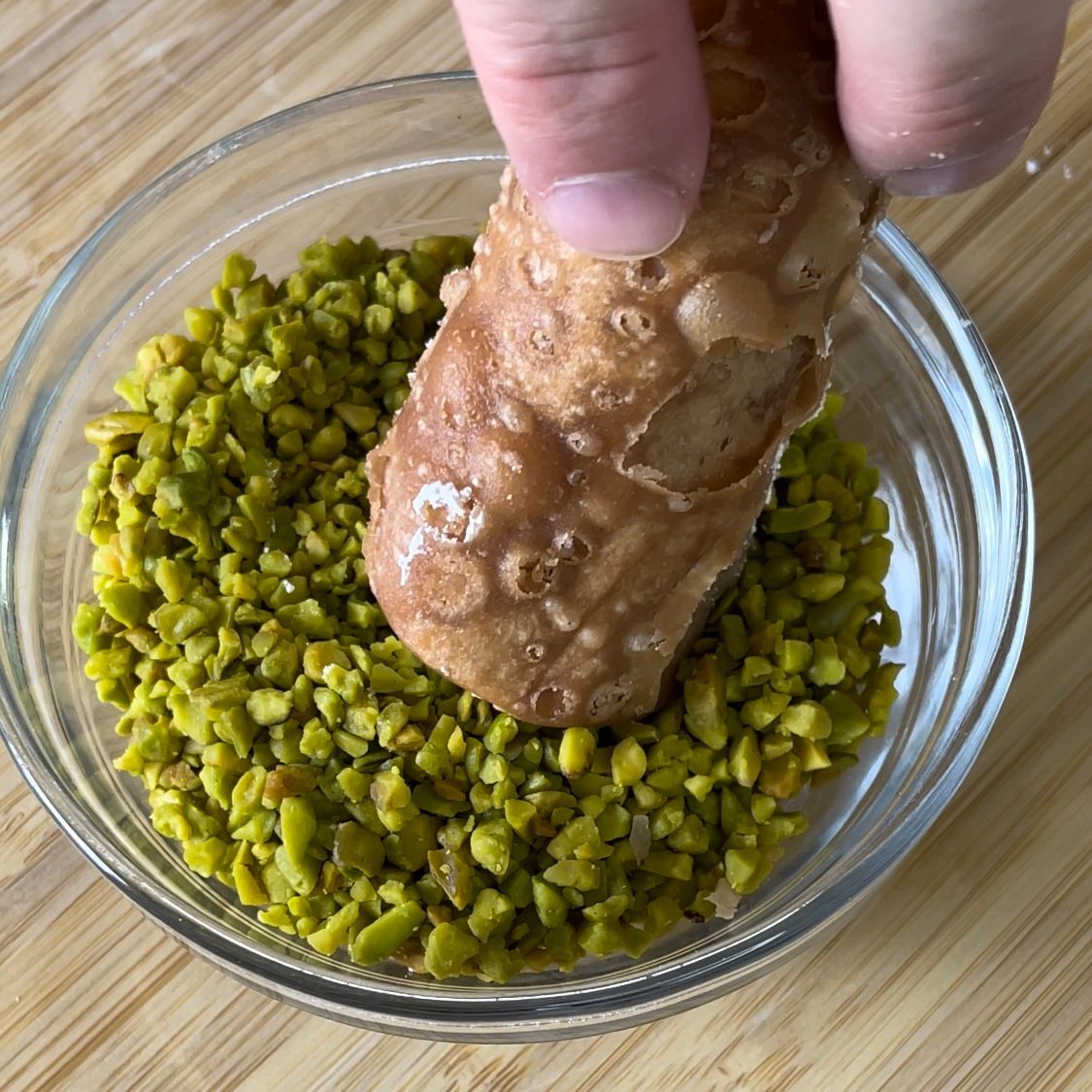 Una persona sta immergendo un cannolo in una ciotola di pistacchi.