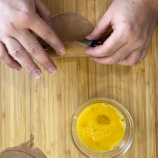 Una persona sta tagliando un pezzo di carta su un tavolo di legno accanto a una ciotola piena di liquido.