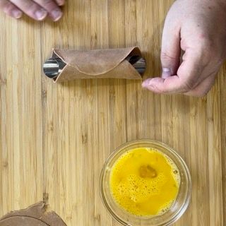 Una persona sta preparando un cannolo su un tavolo di legno accanto a una ciotola piena di liquido giallo.