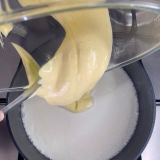 Una persona sta versando un liquido giallo in una pentola di latte.