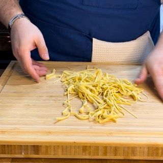 Una persona sta tagliando le tagliatelle su un tagliere di legno