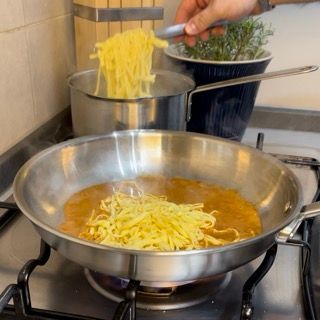 Una persona sta cucinando le tagliatelle in una padella sul fornello