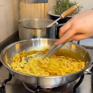 Una persona che mescola i noodles in una padella sul fornello