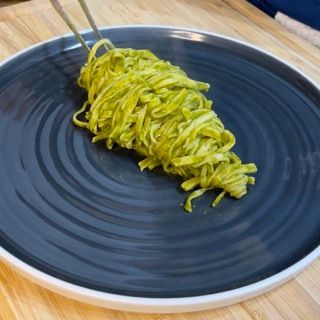 Un piatto nero con sopra spaghetti verdi e bacchette