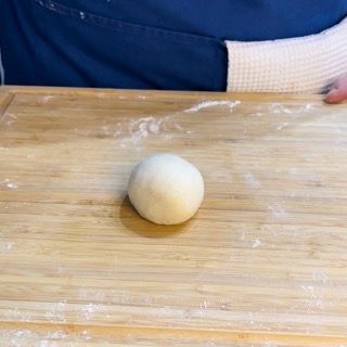 Una palla di pasta è appoggiata su un tagliere di legno.
