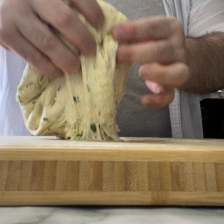Una persona tiene in mano un pezzo di pasta su un tagliere.