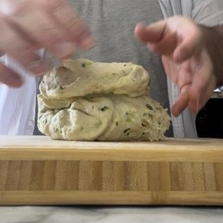 Una persona tiene in mano un pezzo di pasta su un tagliere.