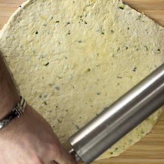 Una persona sta stendendo un pezzo di pasta con un mattarello.