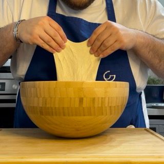 Un uomo con un grembiule sta allungando un pezzo di pasta in una ciotola di legno